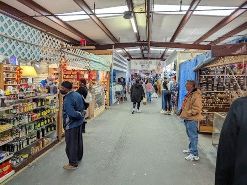 A bustling indoor market with vendors, shoppers, and various goods displayed in stalls along a wide aisle.
