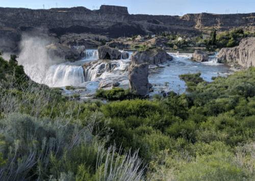 A scenic view of a waterfall cascading over rocks, surrounded by lush greenery and rugged terrain.