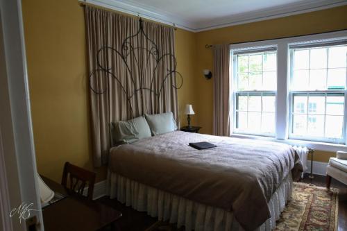 Cozy bedroom with a large bed, decorative wall art, and natural light from windows. A desk is visible in the corner.