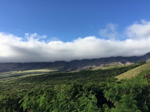Lush green landscape with rolling hills and mountains under a partly cloudy blue sky.