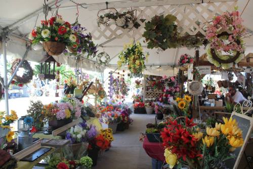 A vibrant flower market under a tent, filled with colorful floral arrangements and hanging decorations.
