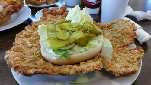 A large fried chicken sandwich with lettuce and pickles on a bun, served on a plate with sides.