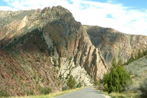 A winding road leads through rugged mountains with colorful rock formations and sparse vegetation under a blue sky.