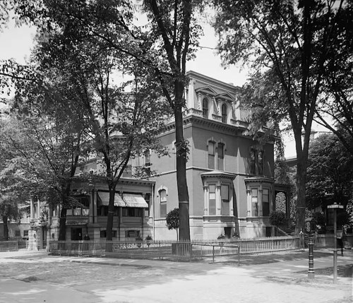 Historic brick building surrounded by trees, featuring ornate architecture and a fenced yard, captured in black and white.