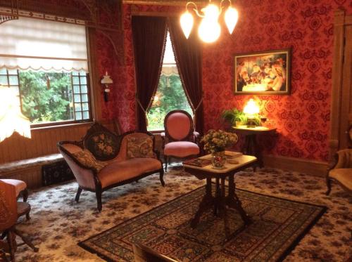 A vintage living room with ornate wallpaper, plush seating, a floral rug, and a table with a vase of flowers.