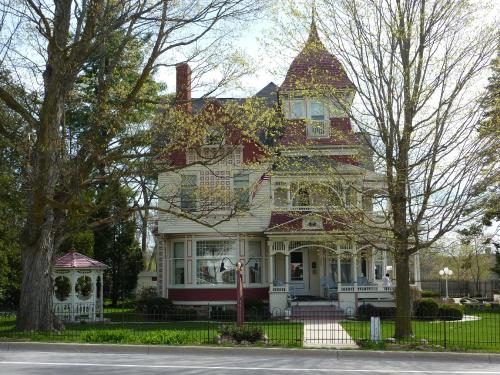 Victorian-style house with a turret, surrounded by trees and a gazebo, on a sunny day.