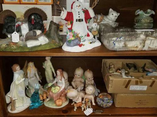A wooden shelf displaying various figurines, including a snowman, turkeys, and dolls, alongside a box of small items.