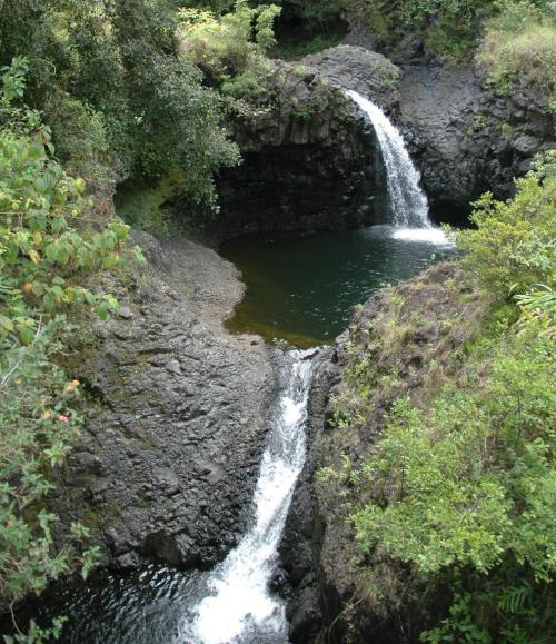 A serene waterfall cascading into a rocky pool, surrounded by lush greenery and natural rock formations.