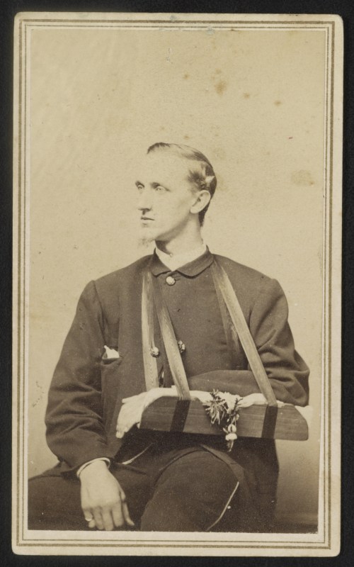 A historical portrait of a man in a military uniform, seated with a wooden arm support and a flower decoration.