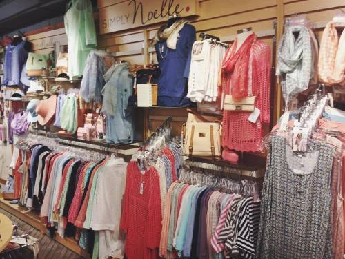 A clothing display featuring various tops, scarves, and accessories on hangers against a wooden wall.