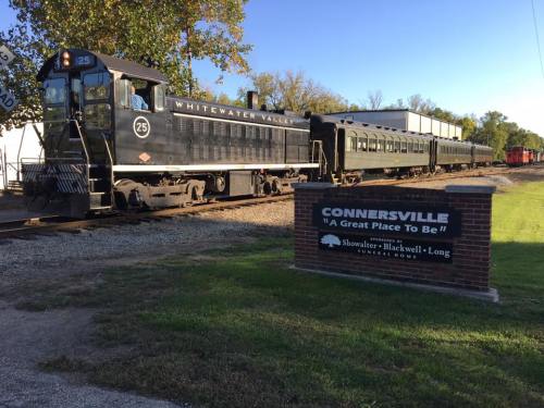 A vintage train at Connersville station, with a sign reading "Connersville: A Great Place to Be!" in the foreground.