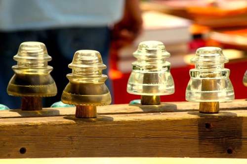 A row of vintage glass insulators on a wooden display, with a blurred background of colorful items.