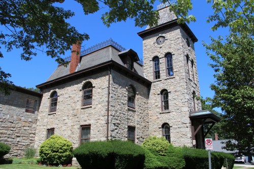 Historic stone building with a tower, surrounded by greenery and clear blue skies.