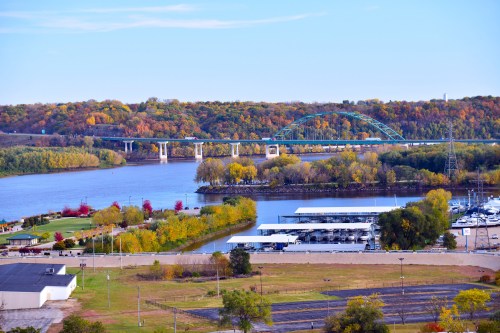 A scenic view of a river with a bridge, surrounded by autumn foliage and a marina in the foreground.