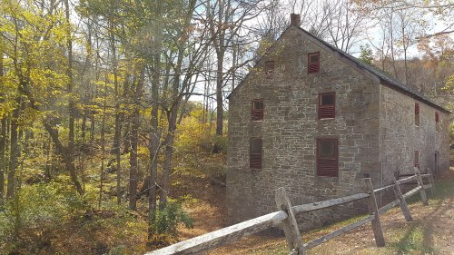 A stone building with red windows surrounded by autumn trees and a wooden fence in a serene, wooded area.