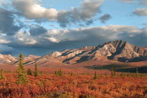A scenic landscape featuring mountains and vibrant autumn foliage under a partly cloudy sky.