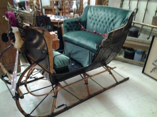 A vintage sleigh with a green tufted seat, displayed in an antique shop.