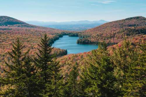 A scenic view of a lake surrounded by colorful autumn foliage and rolling hills under a clear blue sky.