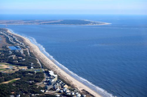 Aerial view of a coastline with sandy beaches, ocean waves, and a distant island on a clear day.