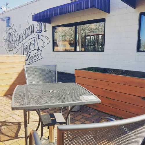 A metal table and chairs on a patio outside a building with a mural and large windows.