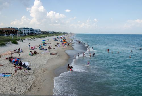 A beach scene with people sunbathing, swimming, and colorful umbrellas along the shore under a blue sky.
