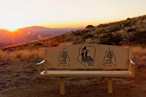 A scenic view of a bench at sunset, featuring a memorial design for the 1971 Mountain Masters.