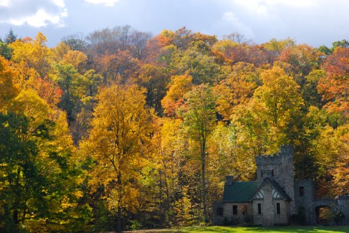 A stone building surrounded by vibrant autumn trees in shades of orange, yellow, and green under a cloudy sky.