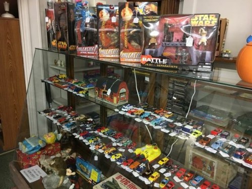 Display case filled with various toy cars, action figures, and collectibles, including Star Wars items.
