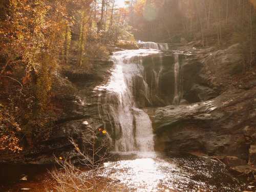 A serene waterfall cascading over rocky terrain, surrounded by autumn foliage and a tranquil pool below.