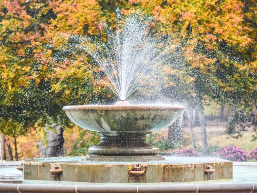 A decorative fountain sprays water, surrounded by colorful autumn foliage.