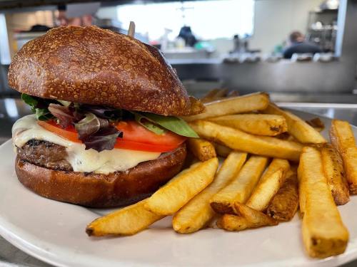 A juicy burger with melted cheese, lettuce, and tomato, served with a side of golden French fries on a white plate.