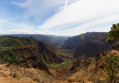 A panoramic view of a lush valley surrounded by steep, rocky cliffs under a blue sky with wispy clouds.
