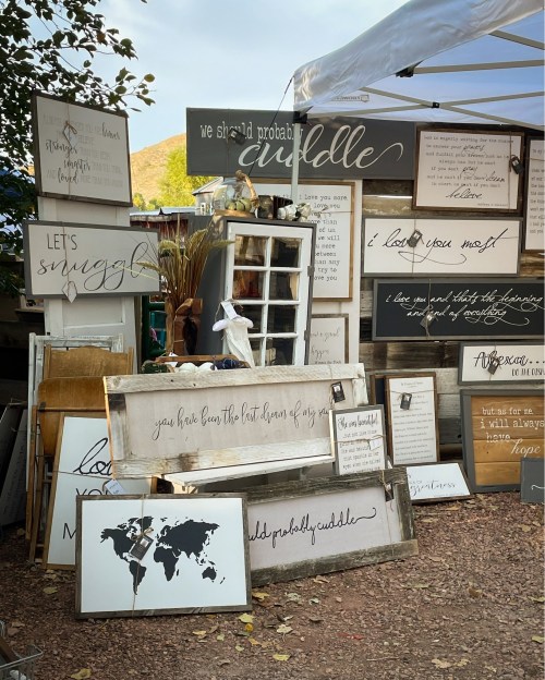 A collection of decorative signs with various quotes and designs displayed at an outdoor market.