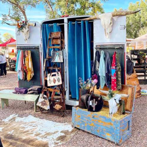 A vintage trailer display with clothing, bags, and decor, featuring cow skulls and colorful fabrics in an outdoor market.