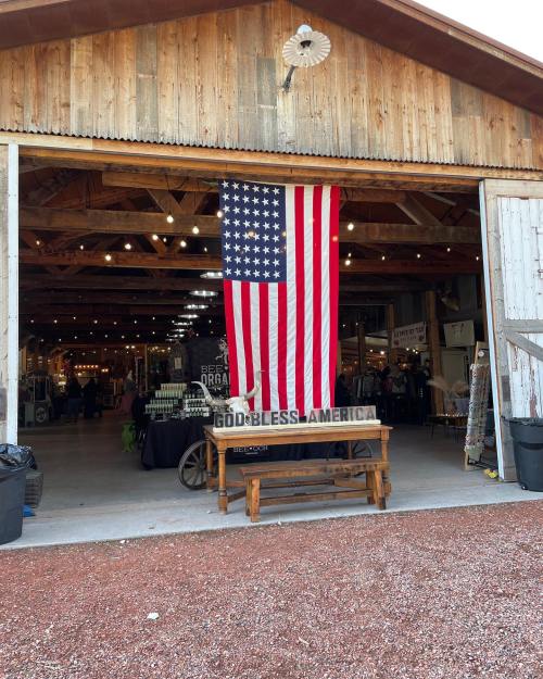 A rustic barn entrance featuring a large American flag and a sign that reads "God Bless America."