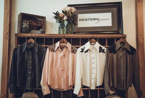 Four stylish shirts displayed on hangers against a wooden backdrop, with a floral arrangement and a sign reading "WESTERN grace."