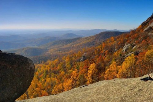 A panoramic view of a colorful autumn landscape with rolling hills and vibrant fall foliage under a clear blue sky.