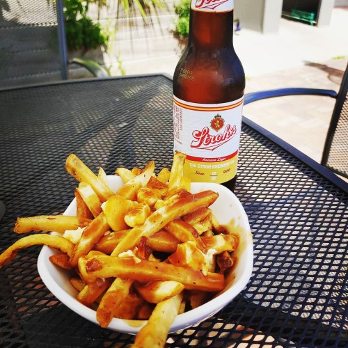 A bowl of golden fries next to a bottle of Strohs beer on a patio table.