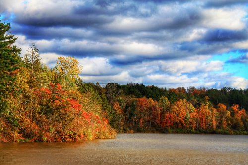 A serene lake surrounded by vibrant autumn foliage and dramatic clouds in the sky.