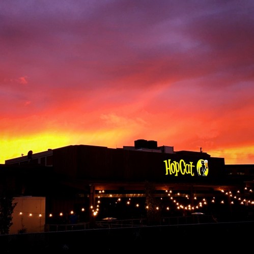 A vibrant sunset casts colorful hues over the HopCat restaurant, illuminated by string lights.