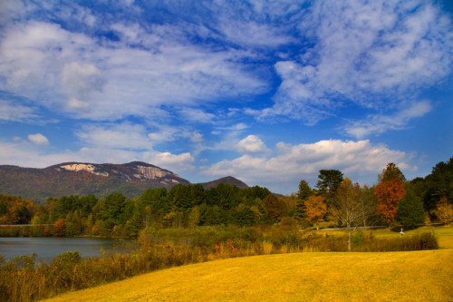 Scenic view of a lake surrounded by autumn foliage and mountains under a blue sky with fluffy clouds.