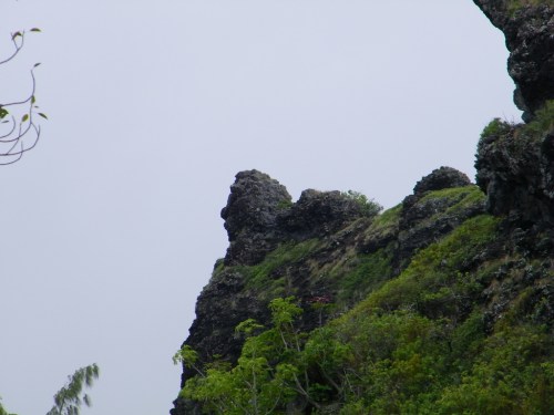 A rocky cliff with greenery on the slopes under a cloudy sky.