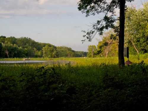 A serene river scene with lush greenery, trees, and a calm waterway under a partly cloudy sky.
