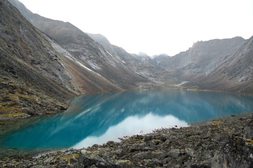 A serene mountain landscape featuring a turquoise lake surrounded by rocky terrain and misty peaks.