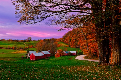 A picturesque autumn landscape featuring vibrant foliage, a winding road, and a red barn under a colorful sunset sky.