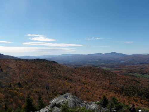 A panoramic view of colorful autumn foliage covering rolling hills under a clear blue sky.