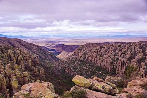 A panoramic view of rugged mountains and valleys under a cloudy sky, showcasing unique rock formations and lush greenery.