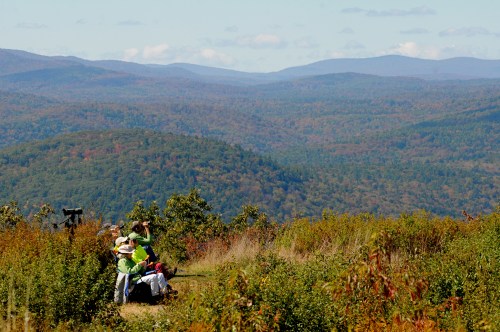 A group of people enjoying a scenic view of rolling hills and colorful autumn foliage.
