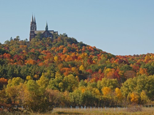 A church atop a hill surrounded by vibrant autumn foliage in various shades of orange, red, and green.