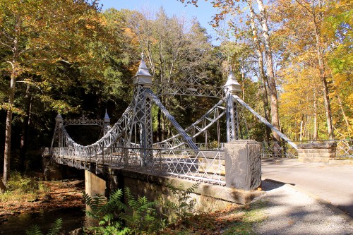 A decorative metal bridge spans a small creek, surrounded by colorful autumn trees.